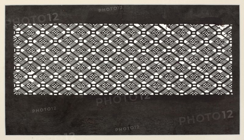 A katagami dyeing stencil for painting kimono, cut into a koshi check ornament with small floral rosettes woven into it, ise-katagami, Japanese art, Japanese culture, ca. 1850 Edo period, Japan, stencil; height 40.1 cm, width 24.3 cm., The image shows a rectangular pattern of repeating geometric cutouts set against a dark background, with a band of intricate latticework near the top and middle and a large darker area below. The lattice consists of a group of diamond-shaped motifs with diagonal striped elements and small floral-like shapes at their centers, creating a grid of connected octagonal and square openings. The predominant colors visible are black, white, and shades of gray, with the white areas forming the cutout pattern and the black and gray tones forming the surrounding background and textured lower field. The overall composition is framed by a narrow lighter border.