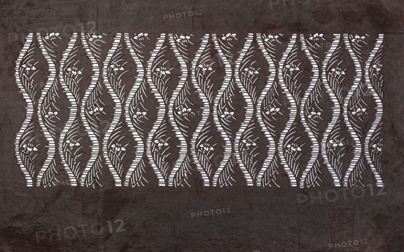 Katagami dyeing stencil; tatewaku wavy clouds pattern with tiny flowers and leaves, geometric and plant patterns, katagami, stencils, Japanese art, Japanese culture, 19th/20th century Meiji period 1868–1912, Japan, stencil, height 40.3 cm, width 24.3 cm, A patterned rectangular panel occupies the center of the image, featuring a repeating wavy lattice of light shapes against a darker background; within each wavy column are stylized floral and leaf motifs. The outer area around the panel shows a textured surface with uneven shading. Visible colors include dark brown, lighter brown, and white, with the white forming the repeating decorative shapes and the browns making up the surrounding textured field.
