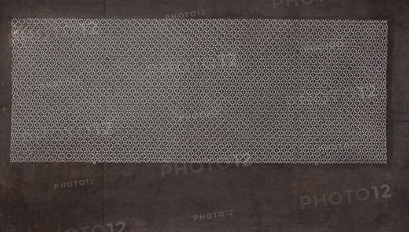Katagami dyeing stencil; geometric pattern made of a dense grid of small rhombuses, Japanese, Meiji period 1868–1912, ise-katagami stencil, geometric ornaments, 19th–20th century, Japan; height 41.0 cm, width 24.1 cm, A rectangular area filled with a repeating small circular and X-shaped pattern in white sits near the top of a darker rectangular background; the patterned area is framed by a wider dark border with visible texture and subtle worn marks, showing colors of black, dark brown, and hints of rust, while the pattern area contrasts in white against a dark backdrop.