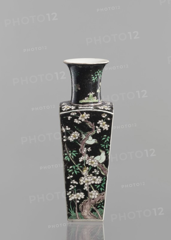 Pair of vases, Chinese, 18th century, colored porcelain famille noire, decorated with birds, plums, and floral motifs; vessel, height 22.5 cm., A tall, narrow vase with a flared rim and a square body sits against a plain gray background; the vase has a predominantly black surface decorated with pale green and white floral motifs and green leaves, pale green birds perched among branches, and brownish branches and trunk details, while the interior of the rim appears off-white.