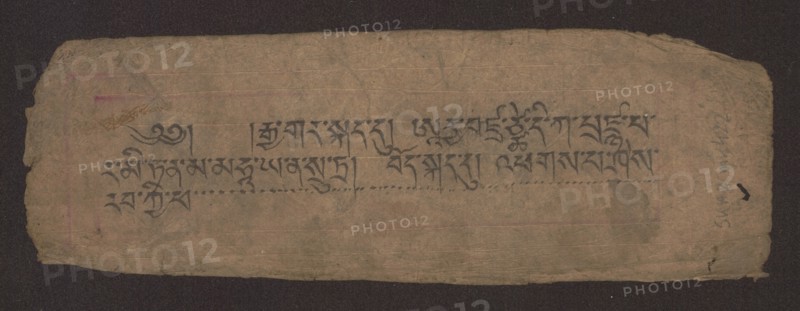 Title page of a Buddhist manuscript of the Diamond Sutra Tib. 'phags pa rdo rje gcod pa zhes bya ba bzhugs+o, unknown creator/scribe, noted, Buddhist art, Tibetan Buddhist art, Tibetan culture, graphic prints, manuscript, sutra, title page in the Péch style, manuscript in the disciple script dbu can, loose pages, unnumbered. Text of the Diamond Sutra Skt. Arya Vajracchedika Prajnaparamita Sutra, translated from Sanskrit, 19th century, Tibet, manuscript; width 22.1 cm, height 7.5 cm, A worn rectangular piece of paper with rough, torn edges placed on a dark background, showing a faded brown-beige surface with visible creases and a few small stains; a group of dark gray-black brush strokes form a horizontal band across the center, and there are faint horizontal guide lines and subtle pinkish and purplish discolorations near the left and right sides; the right edge shows a darker rounded smudge and a small black mark, while the overall texture appears fibrous and aged with variations of ta...