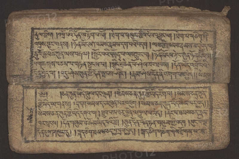 Buddhist text — Commentary on the praise of the names of Manjushri by Ga Rabjampa Kunga Yeshe Tib. 'phags pa 'jam dpal gyi mtshan yang dag par brjod pa zhugs so. Author: Ga Rabjampa Kunga Yeshe Tib. sga rab 'byams pa kun dga' ye shes. Book in Tibetan pecha style, xylographic print in student script dbu can. 26 folios, recto page numbering, first verso, 2 pages missing. Buddhist commentary on the prayer of praise in honor of the names of the bodhisattva Manjushri Tib. 'jam dpal dbyang. Original text from the 15th century; this object dated 19th century, Tibet. Graphics; width 24.6 cm, height 8.0 cm., A worn rectangular object with a faded beige surface bordered by a dark background, showing two horizontal panels separated by a fold. Each panel is framed by a thin dark rectangular border and filled with dense dark markings arranged in horizontal lines. The material appears creased and aged with darker smudges and stains, especially along the edges and fold. The top edge is slightly torn ...