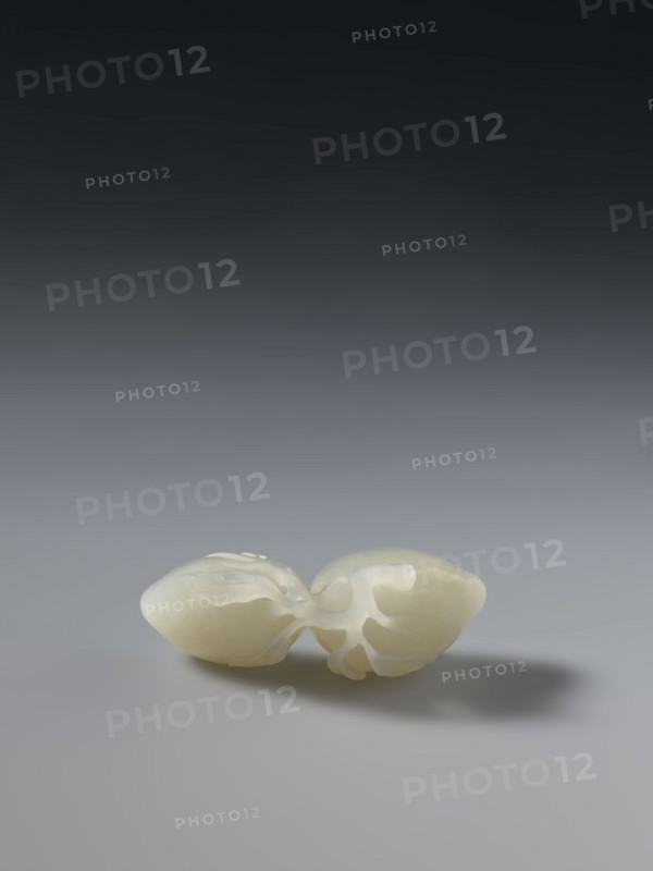 Paperweight depicting peaches; maker, Chinese; Qianlong period 1736–1795, Qing dynasty 1644–1911; materials: glass paperweight; dimensions: height 5.7 cm, width 3.4 cm; iconography: peaches., A smooth, pale cream-colored sculptural object rests on a flat surface, appearing as a pair of connected organic forms with rounded ends and flowing, curved cutouts between them; the object casts a soft shadow to one side on the surface. The background transitions from a mid-gray near the surface to a darker gray toward the top of the image. The visible colors are cream, gray, and dark gray.
