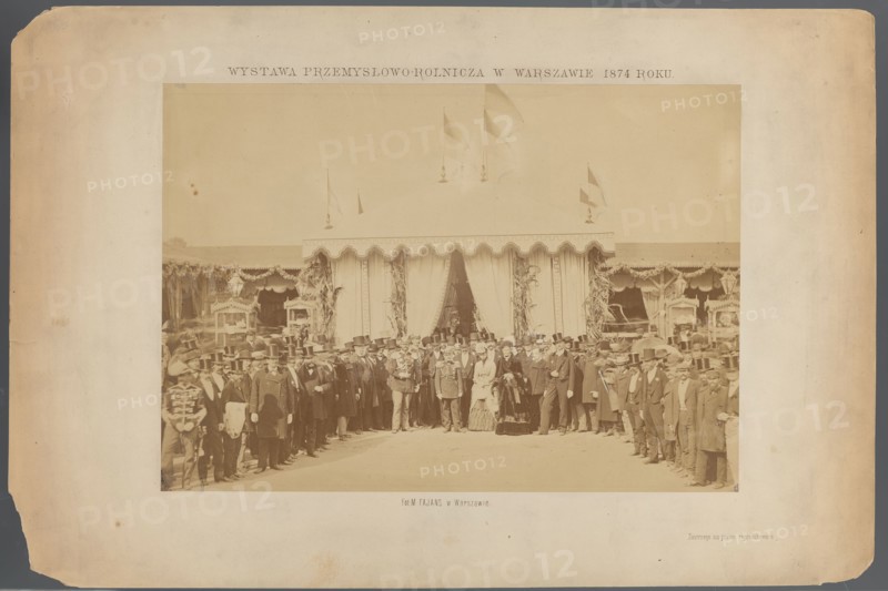 Industrial and Agricultural Exhibition at Ujazdowski Square in Warsaw in 1874. A group of people in front of the Count's pavilion. Ludwik Krasinski during the opening on September 15. Photograph by Maksymilian Fajans 1825–1890. Subjects: exhibition pavilions, Ujazdów Warsaw, industrial and economic exhibitions; persons depicted include Krasinski, Ludwik 1833–1895 and Kotzebue, Pawel 1801–1884. Print glued to cardboard with the entire surface. Date: 15/09/1874, place: Warsaw. Photograph from nature; photographic print: height 26.9 cm, width 17.9 cm; cardboard: height 30.5 cm, width 20.7 cm; passe-partout: height 43.0 cm, width 32.0 cm., A sepia-toned photograph mounted on a faded beige board shows a group of people standing in front of a large decorative tent with scalloped trim and draped curtains; the tent has flags on top and decorative foliage at the entrance. The assembled crowd includes men in dark coats and top hats, a few men in uniforms with visible decorative details, and a fe...