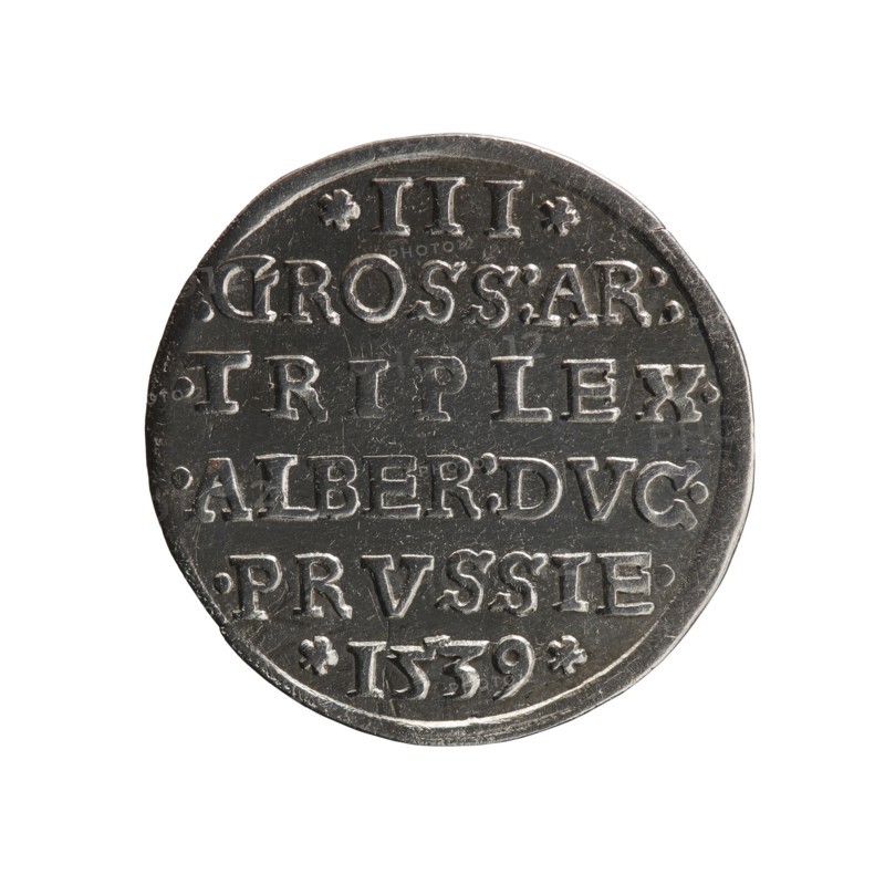 Trojak, Vogelwaider Vogelwaid, Eustachius mintmaster/publisher, Decius, Jost Ludwik fl. 1528–1535 co-creator; mint manager. Albrecht Hohenzollern Prince of Prussia; 1490–1568 — iconography: male busts in armour, stars. Obv.: male bust in armour in profile turned to the right; short hair, beard with sideburns. Inscription around the rim: *ALBER DG MAR BRAN DVX PRVSS. Continuous border with floral motifs between the words. Rev.: in the continuous border an inscription in six lines: *III*/.GROSS:AR:/.TRIPLEX./.ALBER:DVC./.PRVSSIE./*I539* 1539. Ducal Prussia 1525–1701, Königsberg; coin. Diameter 22.4 mm, weight 2.50 g, axis 315°., A round metallic object with a worn, dark silver-gray surface and raised edges sits centered on a white background; the surface shows a series of raised rectangular and curved shapes arranged in horizontal rows, with small decorative raised dots and floral-like marks interspersed, and the metal displays scratches and varied patina with lighter silvery highlights ...