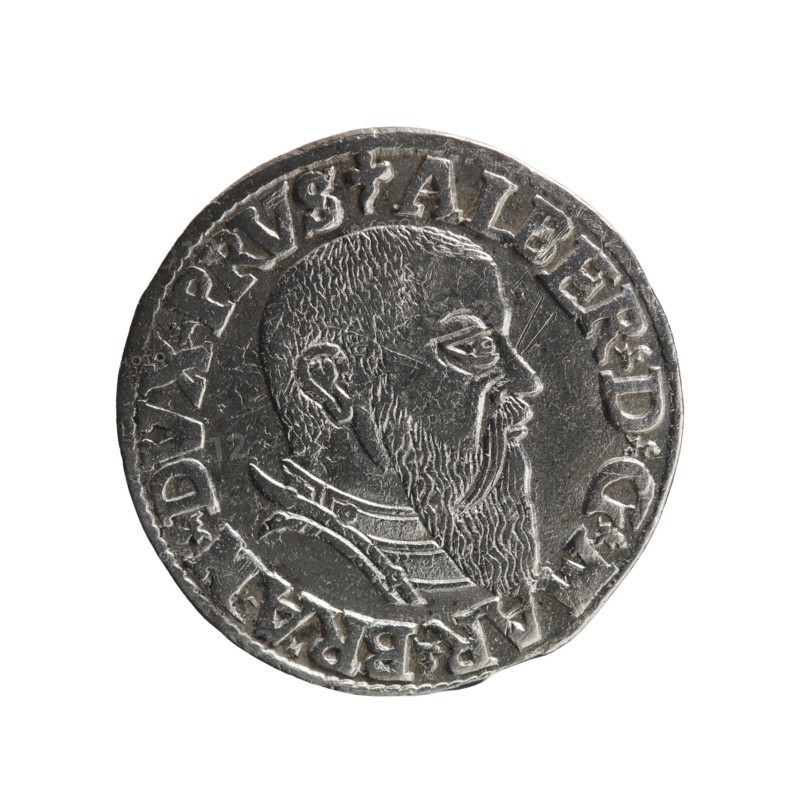 Trojak coin by Schilling, Maciej mintmaster and Decjusz, Jost Ludwik fl. 1528–1535 co-creator; Obverse: male bust in armour in profile to the right; short hair, long beard with sideburns. In the rim an inscription beginning with a trefoil: -ALBER DG MAR BRAN DVX PRVS; pearl border, plant motifs between the words. Reverse: pearl border with a six-line inscription: -III-/.GROSS:AR:/.TRIPLEX./.ALBER:DVC./.PRVSSIE./-1543- with denomination and date between trefoil marks. 1543. Ducal Prussia 1525–1701, Königsberg mint. Coin; diameter 21.2 mm; weight 2.55 g; axis 170°., A circular metallic object with a raised profile of a bearded man facing right, showing detailed hair texture and a long beard, surrounded by raised decorative edging and a ring of raised characters; the surface is silver-gray with darker gray recesses and lighter gray highlights, and the metal shows some wear and small surface scratches.