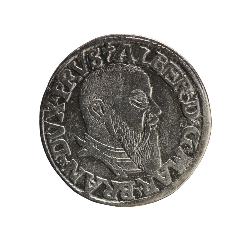 trojak, Schilling, Maciej mintmaster; Decjusz, Jost Ludwik fl. 1528-1535 co-creator; Albrecht Hohenzollern Prince of Prussia; 1490-1568 - iconography: trefoils, male busts in armour. Obv.: male bust in armour in profile turned to the right; short hair, long beard with sideburns. In the rim an inscription beginning with a trefoil: -ALBER DG MAR BRAN DVX PRVS; pearl border, plant motifs between the words. Rev.: in the pearl border an inscription in six lines: -III-/.GROSS:AR:/.TRIPLEX./.ALBER:DVC./.PRVSSIE./-I543-; the denomination and date are between trefoil marks. 1543; Ducal Prussia 1525–1701. Coin: diameter 21.7 mm, weight 2.48 g, axis 225°., A round metallic coin with a raised profile of a bearded man facing right, showing detailed hair and beard texture and a visible ear; the coin surface is silver-gray with darker shadowed recesses and lighter highlights on raised areas; a rim encircles the coin and a decorative band of raised shapes surrounds the portrait; the background is plai...