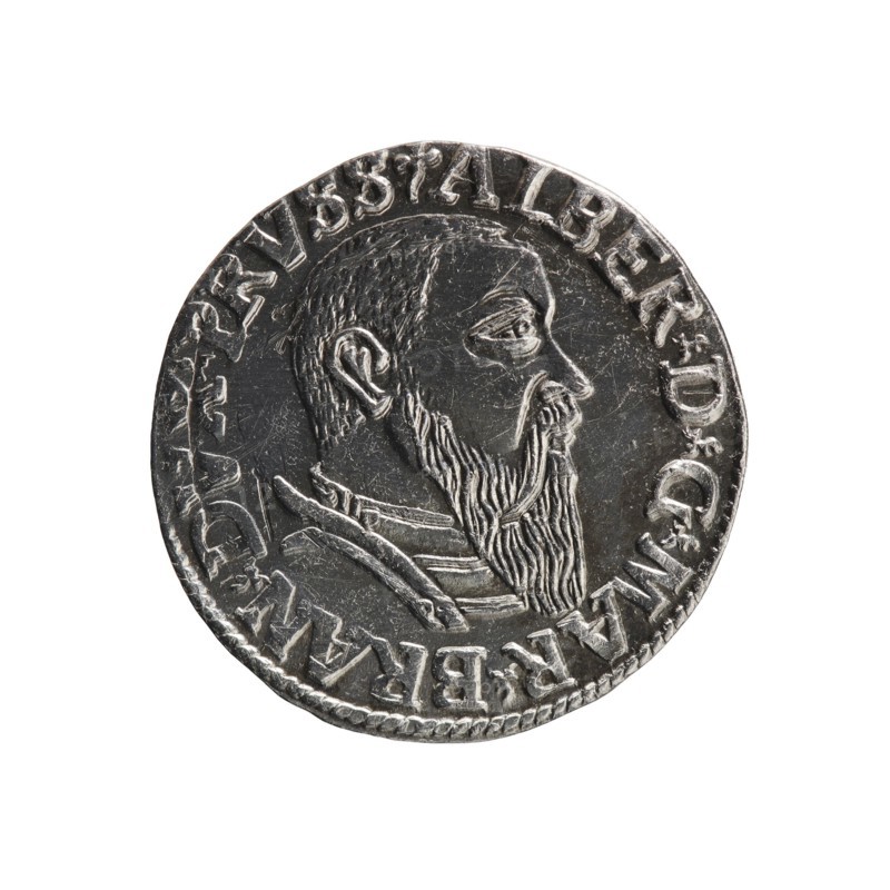 Trojak, Schilling, Maciej mintmaster; Decjusz, Jost Ludwik fl. 1528–1535 co-creator, mint manager. Obverse: male bust in armour in profile to right; short hair, long beard with sideburns; rim inscription beginning with a trefoil: -ALBER DG MAR BRAN DVX PRVSS; pearl border, plant motifs between words. Reverse: six-line inscription in pearl border: -III-/.GROSS:AR:/.TRIPLEX./.ALBER:DVC./.PRVSSIE./-1543-; denomination and date between trefoil marks. 1543. Ducal Prussia 1525–1701, Königsberg mint. Coin; diameter 20.8 mm; weight 2.57 g; axis 200°., A circular metallic object with a raised profile of a bearded man in side view, showing detailed hair and beard texture and a visible ear; the surface has incised lines and wear marks, with a decorative raised rim and a ring of raised characters around the edge. The colors visible are silver and gray with darker gray shadows.