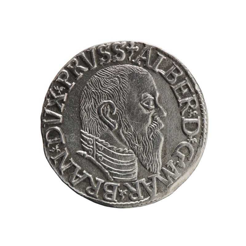 Trojak, Schilling, Maciej mintmaster / publisher, Decjusz, Jost Ludwik fl. 1528–1535 co-creator; mint manager. Albrecht Hohenzollern Prince of Prussia; 1490–1568 — iconography: trefoils, male busts in armour. Obverse: male bust in armour in profile turned right; short hair, long pointed beard with sideburns. In the rim an inscription beginning with a trefoil -ALBER DG MAR BRAN DVX PRVSS, pearl border, plant motifs between the words. Reverse: in the pearl border an inscription in six lines -III-/.GROSS:AR:/.TRIPLEX./.ALBER:DVC./.PRVSSIE./-1544-. The denomination and date are between trefoil marks. 1544. Ducal Prussia 1525–1701, Königsberg mint. Coin; diameter 21.0 mm; weight 2.59 g; axis 200°., A round metallic coin with a raised profile of a bearded man wearing a high, decorated collar, rendered in detailed engraving; the man faces right and has short textured hair and a long beard. The coin surface is silver-gray with darker recessed areas creating contrast. Around the rim is a raised...