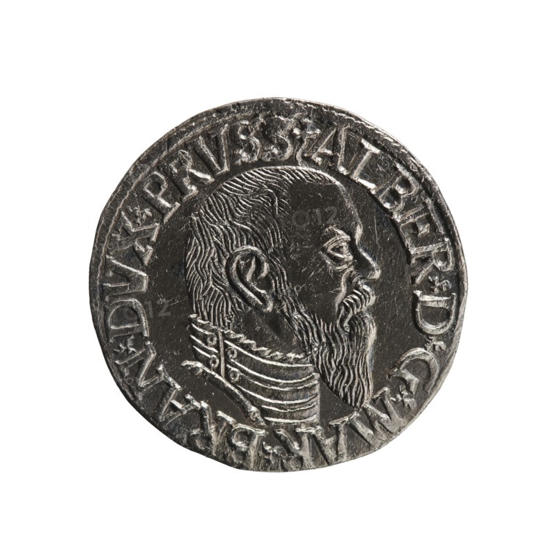 Trojak coin by Schilling, Maciej mintmaster and co-creator Decjusz, Jost Ludwik fl. 1528–1535 mint manager. Obverse: male bust in armour in profile to the right; short hair, long pointed beard with sideburns; rim inscription beginning with a trefoil: -ALBER DG MAR BRAN DVX PRVSS; pearl border; plant motifs between words. Reverse: pearl border with six-line inscription: -III-/.GROSS:AR:/.TRIPLEX./.ALBER:DVC./.PRVSSIE./-I544-; denomination and date between trefoil marks. Dated 1544. Ducal Prussia 1525–1701, Königsberg mint. Coin: diameter 21.2 mm, weight 2.51 g, axis 320°., A round metallic coin with a dark silver-gray surface featuring a raised profile of a bearded man facing right, showing textured hair, a pronounced ear, detailed facial features, and a layered ornamental collar; the coin rim is raised and bears a continuous band of raised markings; visible colors include silver-gray, dark gray, and highlights of lighter silver.