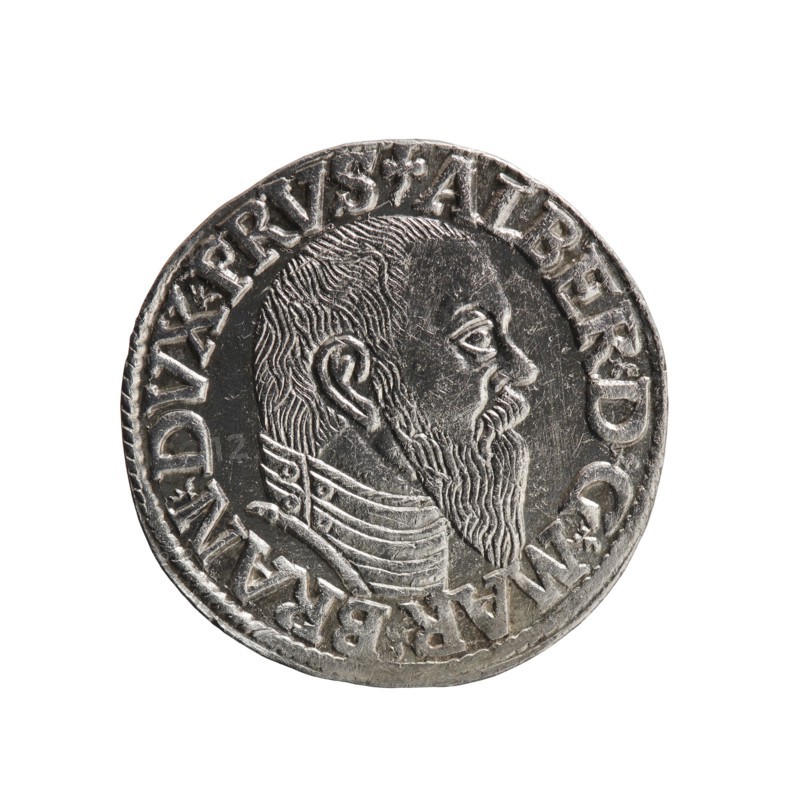 trojak; Schilling, Maciej mintmaster / publisher; Decjusz, Jost Ludwik fl. 1528–1535 co-creator / mint manager. Obv.: male bust in armour in profile turned right; short hair, long pointed beard with sideburns; rim inscription beginning with a trefoil: -ALBER DG MAR BRAN DVX PRVS; pearl border; plant motifs between words. Rev.: inscription in six lines in the pearl border: -III-/.GROSS:AR:/.TRIPLEX./.ALBER:DVC./.PRVSSIE./-I544-; denomination and date between trefoil marks. 1544. Ducal Prussia 1525–1701; Königsberg mint. Coin; diameter 21.2 mm; weight 2.71 g; axis 315°., A circular metallic coin with a raised portrait of a bearded man in profile facing right, showing detailed hair and beard texture and a patterned collar; the coin surface appears silver-gray with darker recessed areas and lighter worn highlights, and a raised rim encircles the portrait.