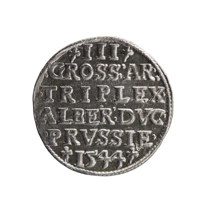Trojak; Schilling, Maciej mintmaster; Decjusz, Jost Ludwik fl. 1528–1535 co-creator. Obverse: male bust in armour in profile to right; short hair, long pointed beard with sideburns; rim inscription beginning with a trefoil: -ALBER DG MAR BRAN DVX PRVS; pearl border, plant motifs between words. Reverse: six-line inscription in pearl border: -III-/.GROSS:AR:/.TRIPLEX./.ALBER:DVC./.PRVSSIE./-1544-; denomination and date between trefoil marks. 1544. Ducal Prussia 1525–1701, Königsberg mint. Coin; diameter 21.2 mm; weight 2.71 g; axis 315°., A circular metallic object with a worn, textured surface appears centered against a white background; it shows raised, blocky carved shapes arranged in horizontal rows across its face, with small decorative marks near the edges and a braided-looking rim; visible colors include silver, dark gray, and hints of black in recessed areas.