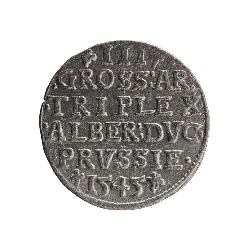 trojak; maker: Schilling, Maciej mintmaster; co-creator: Decjusz, Jost Ludwik fl. 1528–1535, mint manager. Obverse: male bust in armour in profile turned right; short hair, long pointed beard with sideburns; rim inscription beginning with a trefoil: -ALBER DG MAR BRAN DVX PRVSS; pearl border, plant motifs between words. Reverse: inscription in six lines within a pearl border: -III-/.GROSS:AR:/.TRIPLEX./.ALBER:DVC./.PRVSSIE./-1545-; denomination and date between trefoil marks. Date: 1545. Place: Ducal Prussia, Königsberg mint. Coin; diameter 21.2 mm; weight 2.65 g; axis 45°., A round metallic coin with a worn, textured surface shown against a white background; the coin appears silver-gray with darker gray areas in recessed parts and lighter silver highlights on raised edges; the rim is slightly irregular and the surface shows scratches and small dents; there is a pattern of raised linear and blocky shapes arranged across the face of the coin, and decorative small floral-like marks near ...