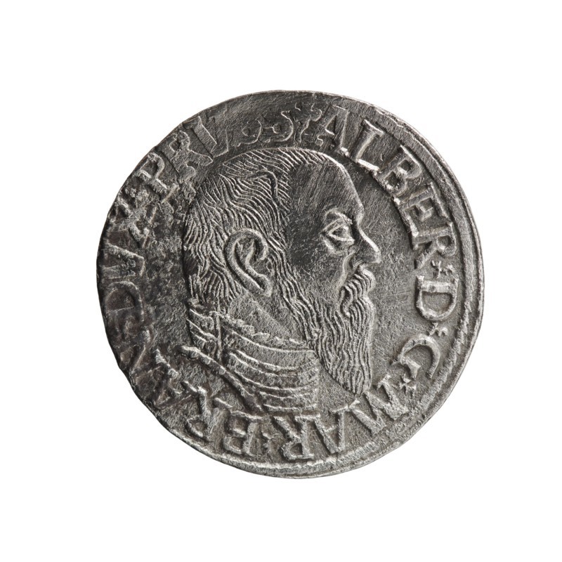 trojak, Schilling, Maciej mintmaster; Decjusz, Jost Ludwik fl. 1528-1535 co-creator; Albrecht Hohenzollern Prince of Prussia; 1490-1568 - iconography: trefoils, male busts in armour. Obv.: male bust in armour in profile turned to the right; short hair, long pointed beard with sideburns. In the rim an inscription beginning with a trefoil: -ALBER DG MAR BRAN DVX PRVSS; pearl border, plant motifs between the words. Rev.: in the pearl border an inscription in six lines: -III-/.GROSS:AR:/.TRIPLEX./.ALBER:DVC./.PRVSSIE./-I545-; the denomination and date are between trefoil marks. 1545. Ducal Prussia 1525-1701, Königsberg mint. Coin: diameter 21.2 mm, weight 2.47 g, axis 315°., A round metallic object with a worn, textured surface showing a raised profile of a bearded man facing right; the profile includes detailed hair, ear, eye, nose, and a long beard, and the figure appears to wear layered clothing or armor at the neck. The object shows raised decorative edges and embossed markings around ...