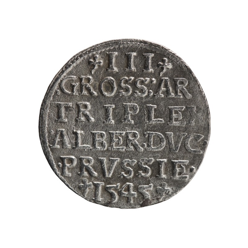 Trojak coin by Schilling, Maciej; co-creator Decjusz, Jost Ludwik fl. 1528–1535. Obverse: male bust in armour in profile to right; short hair, long pointed beard with sideburns; rim inscription beginning with a trefoil: -ALBER DG MAR BRAN DVX PRVSS with pearl border and plant motifs between words. Reverse: inscription in six lines in the pearl border: -III-/.GROSS:AR:/.TRIPLEX./.ALBER:DVC./.PRVSSIE./-I545- with denomination and date between trefoil marks. Iconography includes Albrecht Hohenzollern Prince of Prussia; 1490–1568, trefoils, male busts in armour. 1545; Ducal Prussia. Minted in Königsberg. Coin; diameter 21.2 mm; weight 2.47 g; axis 315°., A round metallic object with a worn, textured surface, showing raised and recessed areas that form patterns; the object has a silver-gray color with darker gray shadows and lighter highlights, and slight tarnish giving subtle brownish and black tones; the edge is uneven and the surface shows indentations and scratches; the background is pl...