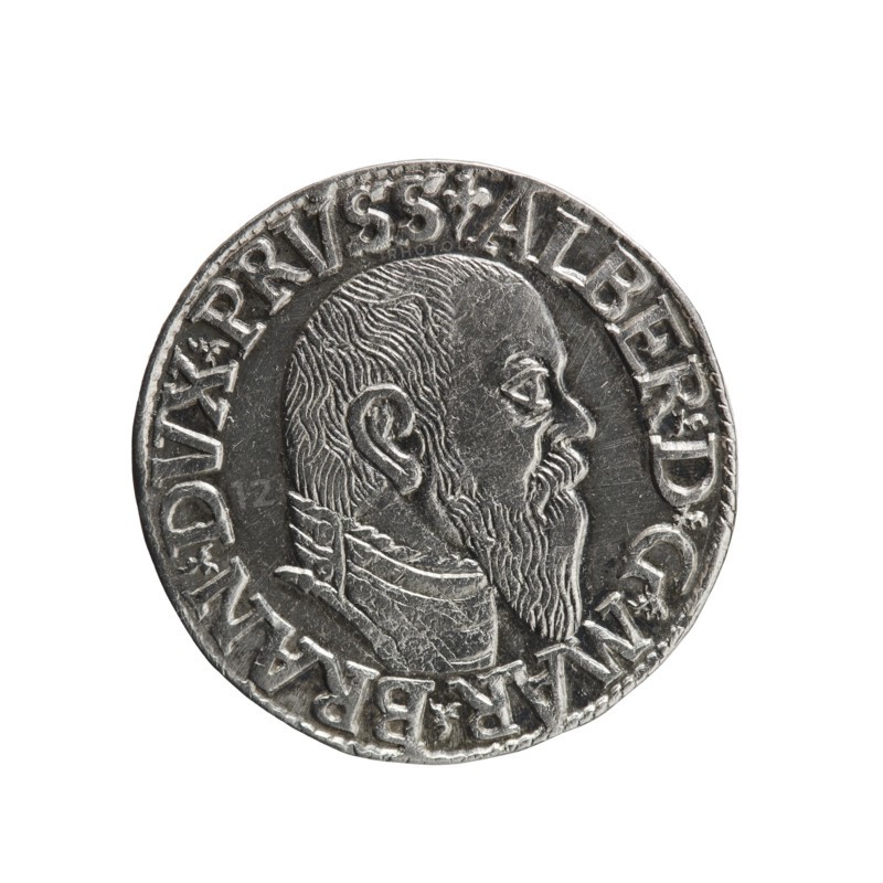 trojak; Schilling, Maciej mintmaster; Decjusz, Jost Ludwik fl. 1528–1535 co-creator; Albrecht Hohenzollern Prince of Prussia; 1490–1568 — iconography: trefoils, male busts in armour. Obv.: male bust in armour in profile turned to the right; short hair, long pointed beard with sideburns. In the rim an inscription beginning with a trefoil: -ALBER DG MAR BRAN DVX PRVSS; pearl border, plant motifs between the words. Rev.: in the pearl border an inscription in six lines: -III-/.GROSS:AR:/.TRIPLEX./.ALBER:DVC./.PRVSSIE./-I545-; the denomination and date are between the trefoil marks. 1545. Ducal Prussia 1525–1701, Königsberg mint. Coin; diameter 21.2 mm; weight 2.70 g; axis 140°., A circular metallic coin with a raised portrait of a bearded man in profile facing right, showing detailed hair and beard texture and a high collar; the coin surface is silver-gray with darker recessed areas and lighter worn highlights, and a ring of raised decorative elements and shapes around the edge.