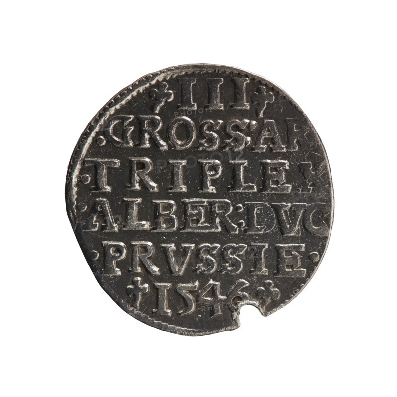 Trojak, Schilling, Maciej mintmaster; co-creator. Albrecht Hohenzollern Prince of Prussia; 1490–1568 — iconography: trefoils, male busts in armour. Obverse: male bust in armour in profile turned right; short hair, long pointed beard with sideburns. In the rim an inscription beginning with a trefoil: -ALBER DG MAR BRAN DVX PRVSS; pearl border, plant motifs between the words. Reverse: in the pearl border an inscription in six lines: -III-/.GROSS:AR:/.TRIPLEX./.ALBER:DVC./.PRVSSIE./-I546-; the denomination and date are between trefoil marks. 1546. Ducal Prussia 1525–1701, Königsberg mint. Coin; diameter 21.1 mm; weight 2.54 g; axis 220°., A round metal coin with a dark gray surface and lighter silver highlights, showing raised lettering and decorative marks across its face, with a small semi-circular notch missing at the lower edge and a lightly textured rim.