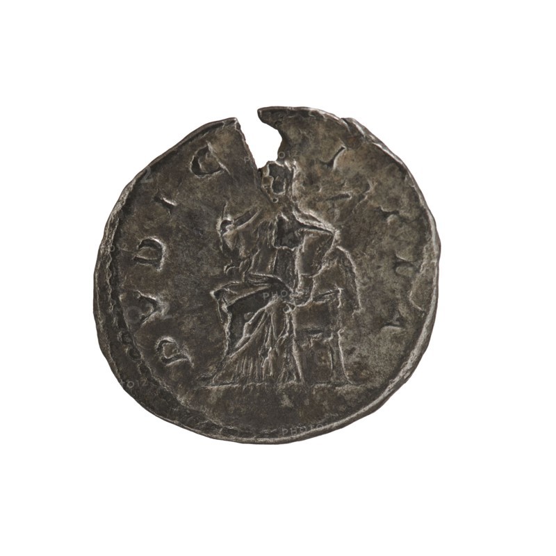Denarius, Elagabalus 204–222; Roman emperor 218–222. Obv.: IVLIAMAE SAAVG — Draped bust of Julia Maesa facing right, pearl border. Rev.: PVDICITIA — Veiled Pudicitia sits on a throne facing left, raising the hem of her veil with her right hand, holding a scepter in her left, pearl border. 218–223. Roman Empire; Rome. Coin; diameter 17.5–18.5 mm; weight 2.15 g., A round worn metallic object with a dark gray to brown patina, showing uneven edges and a small missing section at the top; the surface has raised and recessed areas forming the faint outline of a seated figure draped in cloth, with textured markings around the perimeter and a few lighter and darker patches across the metal.