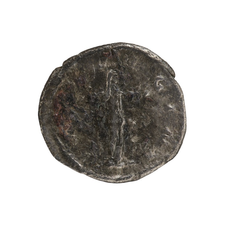 Denarius, Elagabalus reigned 218–222. Issued by Julia Soaemias Augusta, 218–222. Obverse: Draped bust of Julia Soaemias facing right, pearl rim; inscription IVLIASOAEMIASAVGVSTA. Reverse: Juno standing right, holding a sceptre in her right hand and a palladium in her left; pearl rim; inscription IVNO REGINA. Rome, 218–222. Roman Empire. Coin; diameter ~18.0–18.5 mm; weight 2.62 g., A worn round metal object with an irregular edge, appearing mostly dark gray with areas of lighter gray highlights and small patches of reddish-brown discoloration; the surface shows uneven texture with shallow raised and indented areas and a faint vertical raised line near the center.