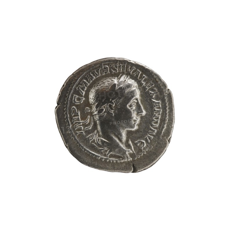 Denarius, Alexander Severus 208–235; Roman emperor 222–235. Obverse: Bust of Alexander Severus right with laurel wreath and paludamentum, pearl rim; inscription IMPCMAVRSEVALEXANDAVG. Reverse: Emperor in military dress standing straight, head turned left, holding a ball in his right hand and a spear in his left; inscription PMTRPIII COSPP. 224, Rome. Roman Empire 27 BC–476. Coin; diameter 20.5 mm; weight 3.25 g., A round metallic coin with a worn surface showing a raised profile of a person's head facing right; the head has short hair and a band or wreath around it, and the neck and shoulders are visible with some drapery. The coin's rim is irregular and slightly dented in places, and there is a raised border around the portrait. The color palette includes shades of silver, gray, and dark gray with subtle highlights and shadows.