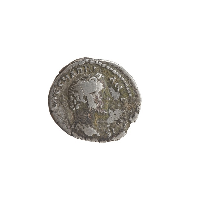 Denarius of Antoninus Pius 86–161; Roman Emperor 138–161. Obverse: bareheaded/uncrowned head of Antoninus Pius to right; inscription IMP T AEL CAES HADRI - ANTONINVS. Reverse: Felicitas standing to left, holding a caduceus in outstretched right hand and a cornucopia in left; inscription AVG PIVS PM TRP COS DES II. Iconography: personifications, caduceuses, cornucopias; Felicitas motif. Date: 138. Place of origin: Rome, Roman Empire. Type: coin denarius. Measurements: diameter 15.5–17.0 mm, weight 3.09 g, axis 165°., A round metal object with an irregular worn edge sits against a white background; the object shows a raised profile of a head in low relief, surrounded by a border of small raised dots and worn surface details, with visible areas of silver, gray, dark gray, greenish patina, and patches of brown.