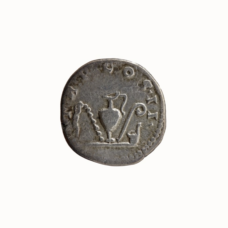 Denarius, Antoninus Pius 86–161; Roman emperor 138–161 issuer. Obverse: Head of Antoninus Pius bare, facing right, legend ANTONINVS - AVG PIVS PP. Reverse: Sacred implements from the left: sprinkler aspergillum, jug capis, crosier lituus and scoop simpulum, legend TR P COS II around. Date: 139. Place of origin: Rome, Roman Empire. Medium: coin. Diameter: 16.5–17.0 mm. Weight: 3.08 g. Axis: 195°., A round metallic object with a worn surface in shades of gray and silver, showing an embossed central motif that includes a vessel-like shape with a handle, a curved element beside it, and a series of rounded bumps forming an arch; the object has an irregular edge and subtle darker tarnish spots against a lighter gray background.