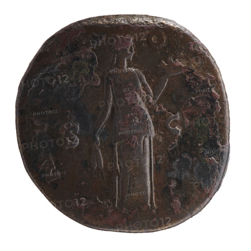 Sestertius of Antoninus Pius 86–161; Roman emperor 138–161. Obverse: head of Antoninus Pius in a laurel wreath to the right; inscription IMP T AEL CAES HADR ANTO - NINVS AVG PIVS PP. Reverse: Fides standing frontally, head turned right; in outstretched left hand a bowl of fruit, in lowered right hand ears of corn; inscription P MTRP - OT COSII, in SC fields. Date: 139. Place of origin: Rome, Roman Empire. Coin; diameter 31.5–32.0 mm, weight 27.27 g, axis 165°., A round, worn coin with a dark brown surface and patches of reddish and greenish discoloration shows a faint raised figure of a standing person in the center holding an object in each hand; the figure is slightly lighter in tone than the surrounding metal. The coin edge is irregular and darker, with areas of rough texture and mottled spots of black and pinkish-red. The background around the figure has uneven dark brown and black areas with scattered small splotches of reddish and green. The overall appearance is aged and corrode...