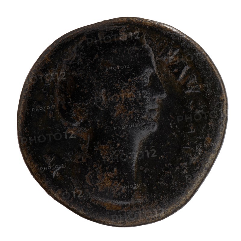 Sestertius; obverse: Bust of Faustina I in drapery facing right, inscription DIVA · FAVSTINA around; reverse: Vesta standing left, in her outstretched right hand she holds a statuette of Athena palladion, in her left a scepter, inscription AVGVSTA all around, in SC fields. Issuer: Antoninus Pius 86–161, posthumous portrait of Faustina the Elder 98–141. Roman deity: Vesta; attribute: palladium, torches. After 141 CE. Roman Empire; Rome. Coin sestertius, diameter 29.0 mm, weight 19.70 g, axis 345°., A round, worn coin-like object with a dark, almost black surface mottled with brown patches and lighter brown corrosion; a faint raised profile of a face in side view is visible against the textured background, with smoother highlights on the cheek and forehead, and a rounded rim that shows subtle variations in dark brown and black tones.