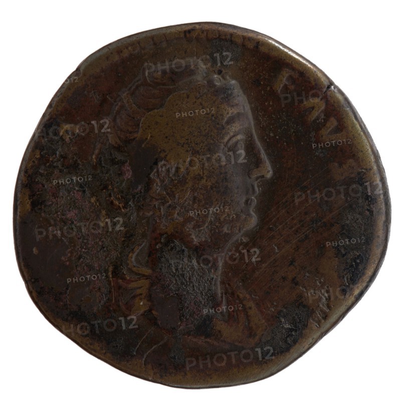 Sestertius, posthumous issue of Faustina the Elder 98–141; Roman empress 138–141, issued by Antoninus Pius 86–161; Roman emperor 138–161. Obverse: Bust of Faustina I draped, facing right; legend A·FAVSTINA. Reverse: Vesta standing left, holding a patera in her outstretched right hand above an altar and a long scepter in her left; legend CONSECRATIO in exergue. Date: after 141. Place of manufacture: Rome, Roman Empire. Medium: coin. Diameter: 31.5–33.0 mm. Weight: 22.65 g. Axis: 180°., A round, worn coin with a raised profile of a person facing right; the surface shows uneven texture and areas of corrosion. The coin displays a patina of dark brown and bronze tones with patches of lighter brown and hints of black and greenish discoloration. The raised portrait and surrounding details are visible in varying relief, with some smoother, shinier spots and other rough, pitted areas. The coin edge is irregular and slightly indented in places.