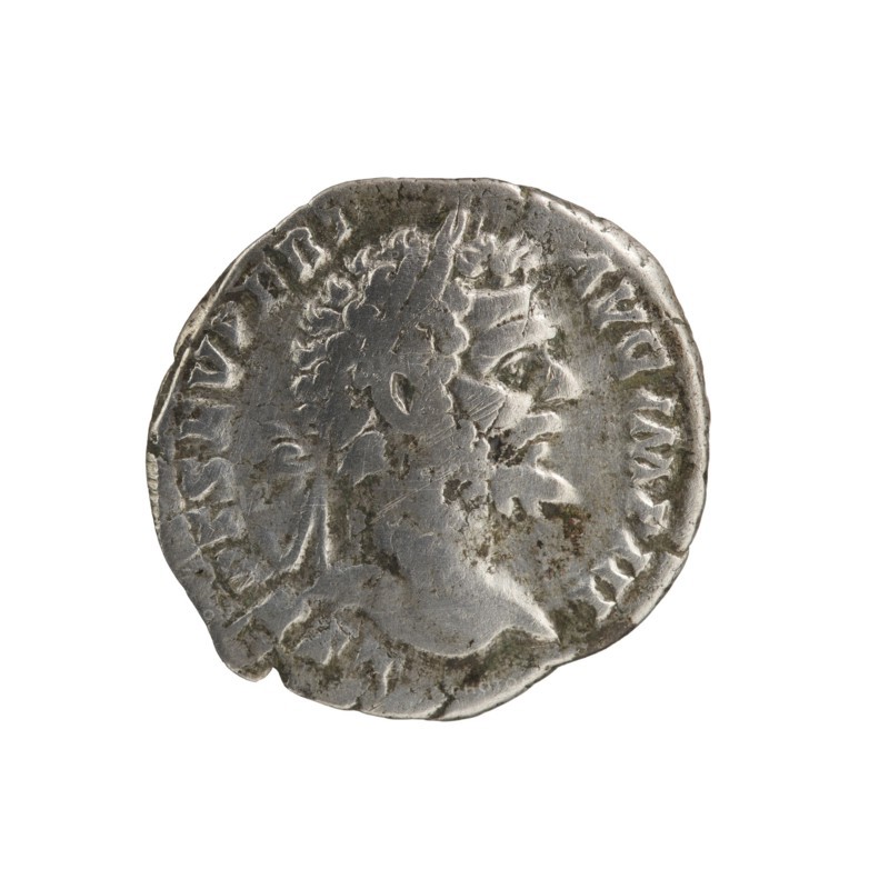 Denarius of Septimius Severus 146–211; Roman emperor 193–211, issuer attributed to Septimius Severus. Obverse: Head of Septimius Severus with laurel wreath facing right, inscription L SEPT SEV PERT - AVG IMP III. Reverse: Pax personified seated left, holding a twig in his outstretched right hand and a cornucopia horns of plenty in his left, inscription PACI AV - GVSTI. Dated 194. Roman Empire, Rome. Coin: diameter 18.0–19.0 mm, weight 2.50 g, axis 0°., A worn round metallic object with a raised profile of a bearded head in relief, showing textured hair and facial features in side view, with visible surface scratches, patina, and areas of darker tarnish; the object appears primarily silver-gray with spots of darker gray and brownish discoloration along the edges and on the face, set against a plain white background.