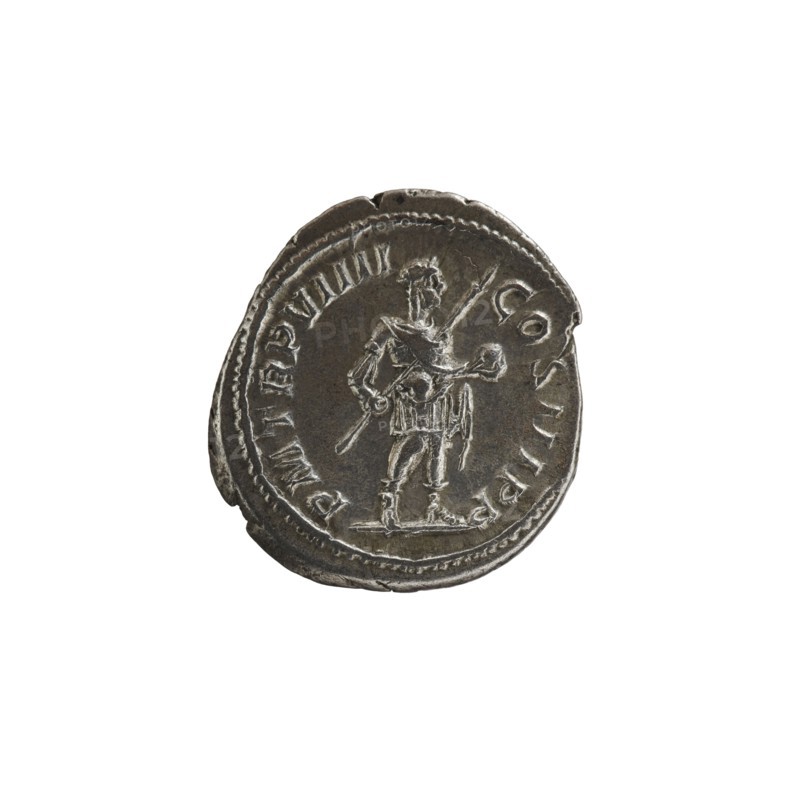 Denarius, Alexander Severus Roman emperor; 222–235 — obverse/depicts standing emperor; iconography includes spears and globes; dated 230; Roman Empire 27 BC–476, Rome; coin; diameter 18.0 mm and 20.5 mm; weight 3.99 g., A circular metallic coin with a worn surface showing a raised depiction of a standing human figure holding a long staff and a smaller object, surrounded by a raised border and worn ornamentation; the coin appears silver-gray with darker gray shadows and lighter silvery highlights, and shows irregular edges and textured wear.