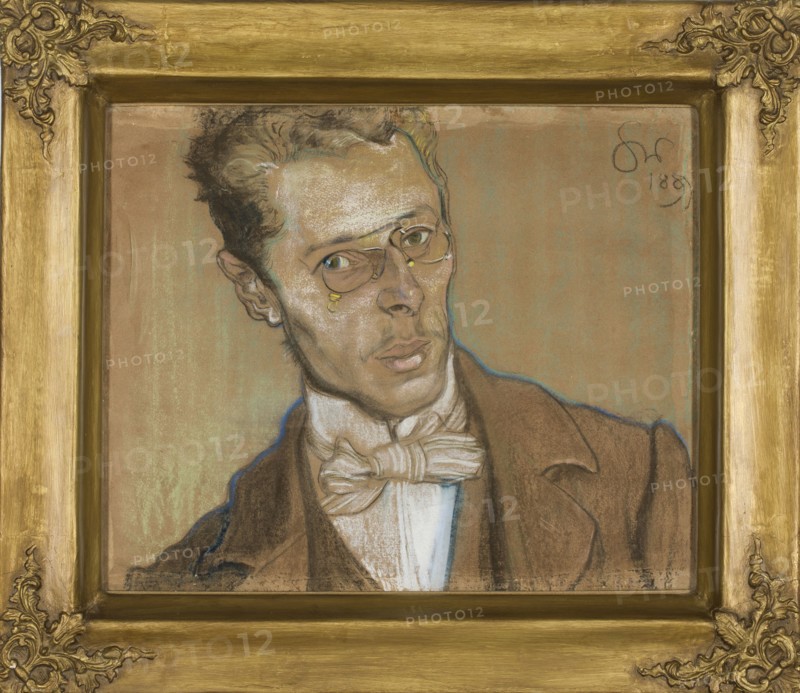 Portrait of Wincenty Parvi, Wyspianski, Stanislaw 1869–1907 author, male portrait, Parvi, Wincenty 1875–1918 — iconography, engineers, Young Poland style, Poland culture, portraits, Polish painting, pastel, drawing, 1899, height 39 cm, width 49.5 cm, A framed portrait of a man shown from the shoulders up wearing a brown jacket and a white shirt with a large bow tie; he has light brown skin and short dark hair with lighter highlights, and he wears round spectacles with small golden accents near the eyes. The man’s face shows subtle shading in beige, brown, and white pastels with outlines in darker tones and a faint blue contour around parts of his silhouette, and his lips and eyes are rendered with muted pink and greenish hues. The background is a flat warm tan color with hints of greenish patina, and the ornate frame surrounding the portrait is a golden color with decorative corner embellishments.