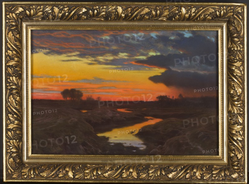 Landscape at Sunset, Jan Grubinski 1874–1945, painter. Pastel on paper, 1909. Subject: sunset landscape, nocturne; style: Symbolism, Young Poland. Medium: pastel; dimensions: height 30.2 cm, width 44.3 cm., testamentary bequest. Poland., A framed landscape painting showing a sunset sky with bands of yellow, orange, red, blue, and dark gray clouds above a darkened horizon; a winding reflective stream runs toward the foreground with golden and bluish reflections, bordered by dark brown and greenish landforms and grasses; a few silhouetted trees stand on the horizon; the painting is set in an ornate gold frame with carved leaf and scroll details and darker shadowed recesses.