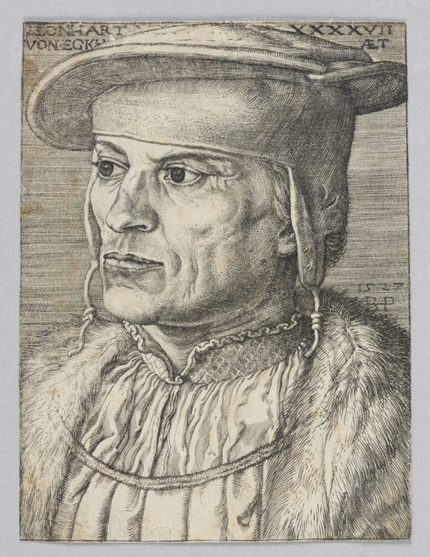Portrait of Leonard Van Eckh by Barthel Beham 1502–1540, German graphic artist. Renaissance-era graphic print, costume design; male bust/portrait. 16th century. Height 10.3 cm, width 8 cm., A detailed monochrome portrait of a man shown from the shoulders up facing left, rendered with fine hatching and line work. He wears a brimmed hat with a rounded crown and a strap hanging down beside his face, and his hair is visible at the ear. His expression appears neutral with prominent eyes, a defined nose, and visible facial lines. He is dressed in layered garments including a textured fur or heavy outer collar and a pleated or gathered inner garment with a decorative neckline. The image palette is black and gray on a light background with subtle aged brownish spots throughout the paper.