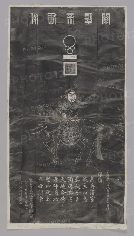 Portrait of the Noble Lord Guan, graphic print, Chinese. Rubbing of stele depicting Guan Yu riding a horse. Title at top: 'Guan sheng di jun xiang' — portrait of Saint Lord Guan (Guan Yu, 160–220), the famous general of the Three Kingdoms Period. Includes one unidentified object (probably 'niu' — a seal with ringed handle) below the title, and the impression of a seal reading 'han shou ting hou zhi yin' — seal of 'han shou ting hou,' a title granted to Guan Yu by Cao Cao (215–220). Depicts Guan Yu wearing a warrior robe, carrying a long-handled knife ('guan gong dao' or 'qing long yan yue da dao'), riding a horse ('chi tu ma', the famed speedy horse given to him by Cao Cao). Inscriptions on the lower left corner. Painting by Li Jintai (Qing artist) copying a model painting. Beginning of the 20th century, China, Xi'an. Graphic print; height 117.0 cm, width 63.0 cm.
