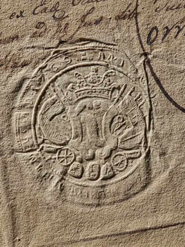 Seal of Antoni Weglenski, Starost of Chelm. Antoni Weglenski (fl. ca. 1769); Witold Zurakowski (?-1927). Document seal; coat of arms seal; Szreniawa coat of arms; private seal; seal of a starost. Round, dry impression of the seal of Antoni Weglenski, Starost of Chelm. On the decorative shield the Szreniawa coat of arms, behind the shield rich panoplies. Partially illegible inscription on the rim: 'ANTON, CAPITANEUS AD 1769'. 1769, Poland., A textured beige paper surface with an embossed circular seal featuring a crowned emblem in the center, surrounded by ornamental shapes and curved bands; there is dark brown ink handwriting partly visible near the top and right edges, and the overall colors visible are beige, tan, brown, and darker brown shading.