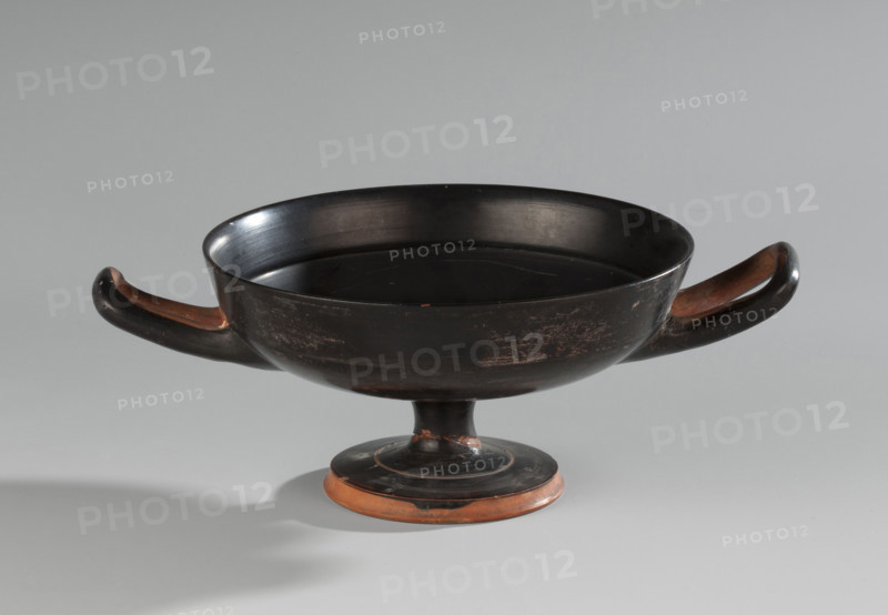 Black-finned kylix, Vicup type. Vicup type kylixes are characterized by a straight edge and a concave outer wall of the foot, which has a reserved surface. The lower surface of the foot is concave, decorated with a wide band of black varnish. The vessel has two handles mounted at the level of the rim. Technology: entire surface covered with an evenly distributed, glossy black varnish of good quality. Traces of turning visible under the varnish. Clay is cleaned. Comments: surface dirty, with visible chips, scratches, and abrasions. Fragment of the foot is glued on. Visible conservation additions. Clay color: 2.5 YR 6/6 (light red). Varnish color: 10 YR 2/1 (black). Ca. 480 BC (ML Bernhard dates the monument to ca. 480 BC). Attica. Vessel: kylix. Height 7.6 cm; width 20.7 cm; depth 14.2 cm; weight 0.210 kg.