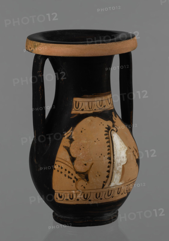 Red-figure pelike, Attic workshop; pelike (vessel), pink clay. Slightly matte black engobe. Some elements painted white. Pelike with a slender belly, wide neck widening upwards. Rolled outward rim decorated with a frieze of ox-eyes. Two bipartite handles attached vertically below the rim, extending to the gently sloping shoulders. On either side of the body, two scenes bounded top and bottom by an ox-eyes frieze. Kerch style. Scene A: Woman's head turned right, wearing a Phrygian cap whose edge is marked with a black line with elongated points; face and neck painted white. In the background on the right, a horse protoma; on the left, the front part of a griffin. Scene B: Two male figures facing each other, wrapped in long cloaks; facial features unmarked. Preservation: partially reconstructed rim. Date: 2nd half of the 4th century BC. Origin: Attica. Dimensions: height 29.9 cm, width 13.1 cm.