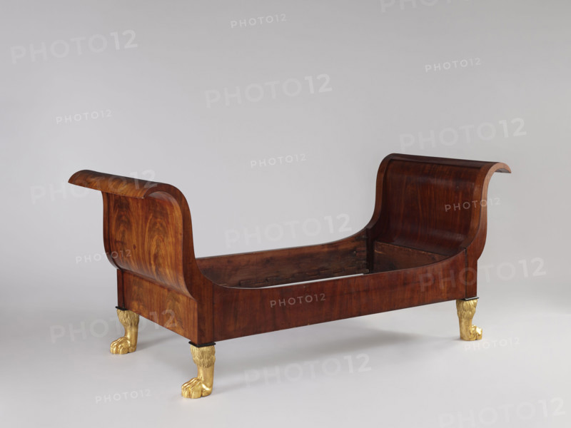 Bed with animal-paw legs, Empire style, mahogany, c. 1815–1830. S-shaped outward-curving pediments of equal height and straight side boards; supported by four carved, gilded legs in the form of furry animal paws. Pediment frames with single panels, strong upturns at the top and simple bottoms, connected to the sides with screws and hooks. Upper corners of the sides arch into the pediment frames; inner bottom edges have glued-on toothed strips supporting the cross slats under the mattress. One pediment veneered on the outside with ash-stained mahogany. Bedrooms; Warsaw, Central Europe. Height 103 cm; width 192 cm; depth 94.5 cm.
