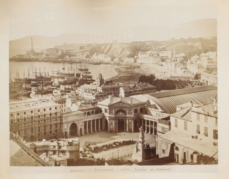 Genova panorama dalla scuola di marina, View of the harbor, the marine school and the station of Genoa, Italy, album page, photograph, This photo is part of an album., Genoa, 1870 - 1890, photographer, paper, albumen print, height 217 mm x width 275 mm, harbor, city-view in general, 'veduta', station, shelter (railway, tramway), A wide coastal cityscape viewed from above showing a semicircular plaza with a grand colonnaded building and a sculpted fountain in front, rows of parked carriages and shaded seating around the square, adjacent multi-story buildings with shuttered windows and tiled roofs, a long arched train shed roof visible behind them, a busy harbor filled with numerous masted sailing ships and reflections on calm water, a promontory with a tall lighthouse and clustered buildings, terraced hills and cliffs rising behind the shoreline, scattered villas and larger buildings on the hillside, tree-lined areas and patches of open ground, and a pale sky above the entire scene.