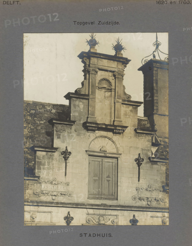 Town Hall. Gable South side, Stepped gable of the town hall in Delft, photograph, number: '52', inscription: 'The right of reproduction of these photos is reserved by the Publisher.', inscription: 'Delft. 1620 and 1760.', Delft, c. 1900 - c. 1904, photographer, paper, pasteboard, gelatin silver print, height 157 mm x width 118 mm, town hall, decorated gable, Stadhuis (Delft), A sepia-toned photograph shows the upper portion of a stone building facade with ornate architectural details. The central section features a pedimented gable with carved scrolls and a recessed arched niche topped by a shell motif, flanked by vertical pilasters and cornices. A double wooden door with simple recessed panels sits below a semicircular arch. Decorative iron fleur-de-lis wall mounts project from the masonry on either side of the facade. Stone plaques with ornate surrounds are set into the wall at mid height. A slate-tiled roof slopes down to the left, and to the right a taller stone chimney or tower ri...