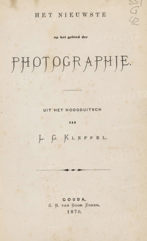 The latest in the field of photography, book, writer (clerical worker): LG Kleffel, Berlin, publisher: GB van Goor & Zonen, Gouda, 1870, writer (clerical worker), pasteboard, paper, textile materials, letterpress printing, height 185 mm x width 125 mm x thickness 13 mm, A faded, aged page with a cream background and scattered brown foxing spots, centered ornamental line and decorative flourish, and several lines of printed text in varying typographic styles and sizes arranged vertically down the page, with stylized large lettering near the top and smaller lines and a signature-like line in the middle, plus a cluster of small handwritten pencil marks along the top right edge.