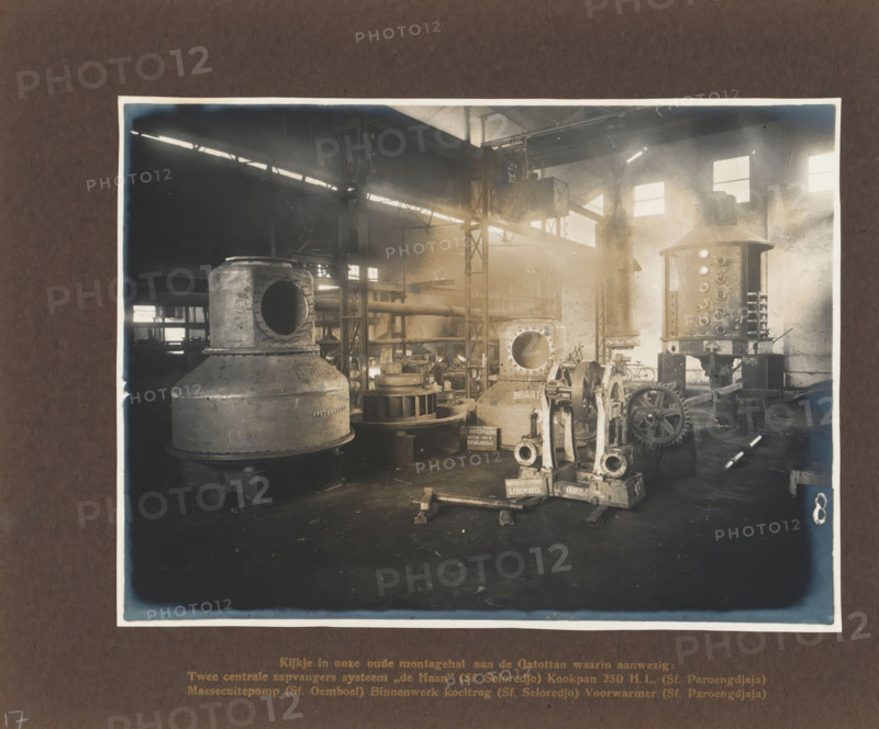 A glimpse into our old assembly hall on the Gatottan ..., album page, photograph, Album page with a photo of a factory hall containing various machines. Manufactured by Machinefabriek Braat and intended for the Seloredjo, Paroengdjaja, and Oemboel Sugar Factories, 1923. Part of the photo album Machinefabriek Braat Soerabaia-Djocja-Tegal, ca. 1916-1924., Surabaya, 1923, photographer, Java, East Java, paper, pasteboard, matte daylight collodion silver print, height 170 mm x width 231 mm, height 240 mm x width 290 mm, Person, NV Machinefabriek Braat, Oemboel Sugar Factory, Seloredjo Sugar Factory, Paroengdjaja Sugar Factory, colonial system, factory-interior, machine shop, machines, parts of machines, tools and appliances, economic history, overseas history, sugar industry, company history, Period, 1916 - 1924, The image shows the interior of an industrial workshop with large metal machinery and equipment arranged across the floor, including cylindrical tanks with round openings, a vertic...