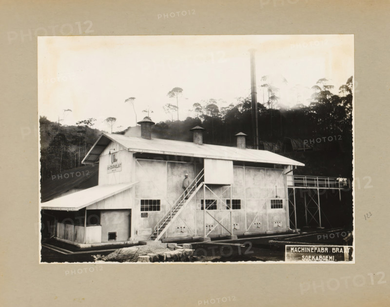 Daradjat Cinchona Enterprise, album page, photograph, Album page with a photograph of a building of the Daradjat cinchona enterprise, built in 1935 by Braat Soekaboemi. Part of a photo album with photographs of machines and constructions of the NV Machinefabriek Braat in Surabaya, Soekaboemi, and Tegal from the period 1931-1937., West Java, 1935, photographer, Java, paper, pasteboard, gelatin silver print, height 165 mm x width 232 mm, height 250 mm x width 320 mm, Person, NV Machinefabriek Braat, factory-building, economic history, overseas history, company history, cinchona cultivation, Period, 1931 - 1937, A black and white photograph of an industrial building with a corrugated metal roof and three cylindrical vents protruding from the rooftop, a tall vertical smokestack rising behind the structure, a set of exterior stairs leading to an upper doorway with a person standing on the landing, multiple small rectangular windows along the building facade, structural support beams and a r...
