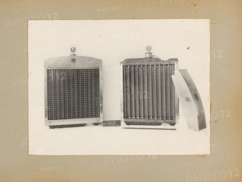 Radiator for roller, album page, photograph, Album page with a photo of the front and back of a radiator for a roller. Part of a photo album with photos of machines and constructions of the NV Machinefabriek Braat in Surabaya, Sukabumi and Tegal from the period 1931-1937., Java, 1931 - 1937, photographer, paper, pasteboard, gelatin silver print, developing gelatin silver print, height 166 mm x width 222 mm, height 250 mm x width 320 mm, Person, NV Machinefabriek Braat, machines, parts of machines, tools and appliances, economic history, overseas history, company history, Period, A photograph mounted on a beige backing shows two metal radiators displayed side by side on a white background with a curved metal panel leaning against the right radiator; each radiator has a circular ornament on top, fine vertical cooling fins, and a rectangular frame, and a small rectangular plaque sits below the radiators on the surface.