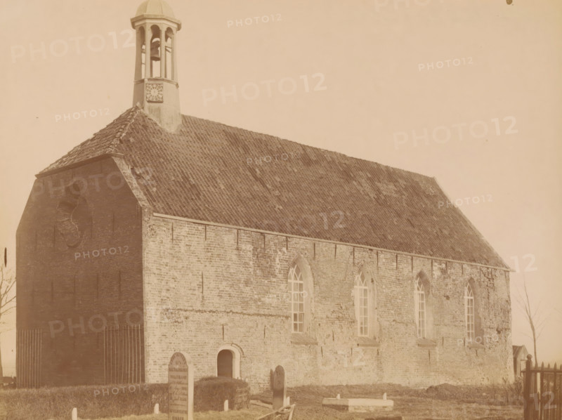 View of the Reformed Church in Rottum, photograph, annotation: 'Rottum, gem. Kantens', annotation: 'NH church in Rottum, Rottum, 1890 - 1910, photographer, Attributed to, paper, pasteboard, albumen print, height 174 mm x width 231 mm, church (exterior), A sepia-toned photograph of a brick building with a steep tiled roof and a small belfry rising from the roofline, the belfry showing open arches and a visible bell, the building’s side wall featuring tall arched windows and a lower arched doorway, the foreground showing a grass area with several upright gravestones and a low rectangular grave marker, and a simple wooden fence visible at the right edge.