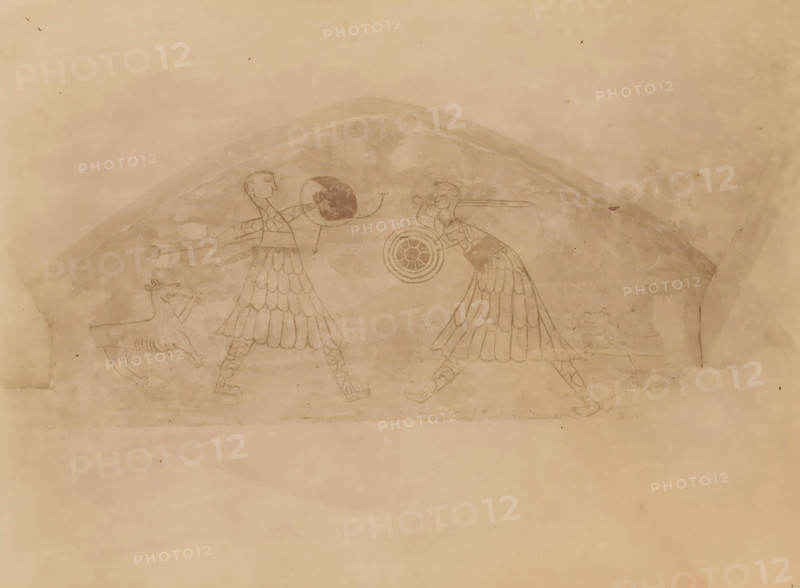 Mural in the Reformed Church in Westerwijtwerd, photograph, annotation: 'Church in Westerwijtwerd, NW view July 1897, municipality of Middelstum', annotation: 'Mural in the Dutch Reformed Church in Westerwijtwerd, Found and whitewashed again in 1897, See Hoogewerff I, p 46-50, photo July 1897, Westerwijtwerd, 1897, photographer, Attributed to, paper, pasteboard, albumen print, height 163 mm x width 222 mm, painting (including book-illumination, miniature-painting) (mural painting), A faded wall scene shows two stylized human figures facing each other, each wearing patterned garments with layered skirt shapes and leg coverings with diagonal markings; the figure on the left holds a long horizontal object and extends an arm toward a circular shield-like form with a darkened semicircular area, while the figure on the right holds a round, concentric shield and has an elongated object projecting from behind the head; two animal figures appear near the lower edges, one near each human, depict...
