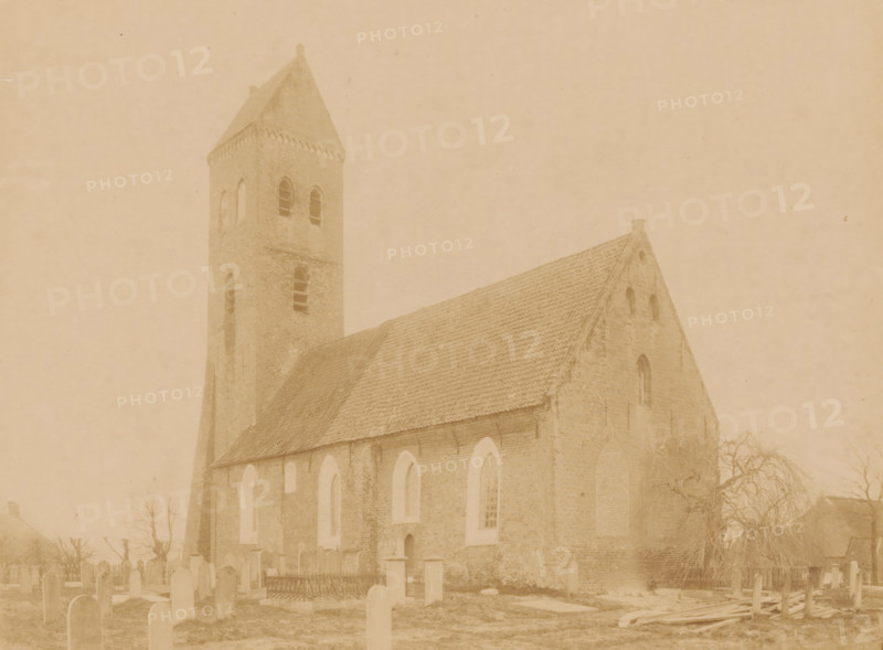 View of the Reformed Church in Midwolde, photograph, annotation: 'Midwolde', annotation: 'Kerk v, d Ned. Rev. avg. in Midwolde, April 1897', Midwolde, 1897, photographer, Attributed to, paper, pasteboard, albumen print, albumendruk, height 164 mm x width 218 mm, churchyard, cemetery, church (exterior), A sepia-toned photograph shows a brick church with a steep tiled roof and a square bell tower topped by a pointed roof, the tower featuring tall arched window openings. The church wall displays a series of tall arched windows and a small doorway, and the gable end has a small circular opening near the roof peak. In front of the church is a graveyard with upright headstones and a fenced plot, and a leafless tree stands near the right side of the building. The scene appears faded and evenly tinted, with soft contrast and visible texture on the brickwork and roof tiles.