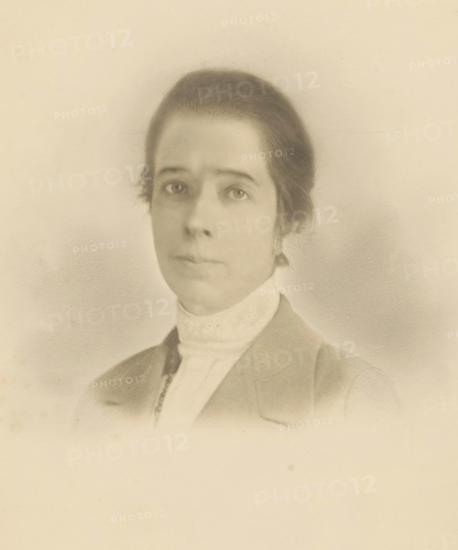 Portrait of unknown woman, photograph, photographer: circle of Cornelia Hendrika Jonker, 1880 - 1920, paper, pasteboard, gelatin silver print, developing gelatin silver print, height 240 mm x width 178 mm, height 235 mm x width 174 mm, historical persons - BB - woman, A faded sepia portrait of a person shown from the shoulders up, with hair pulled back and a high lacy collar visible beneath a jacket, soft shading around the face, neutral expression, and a plain light background.