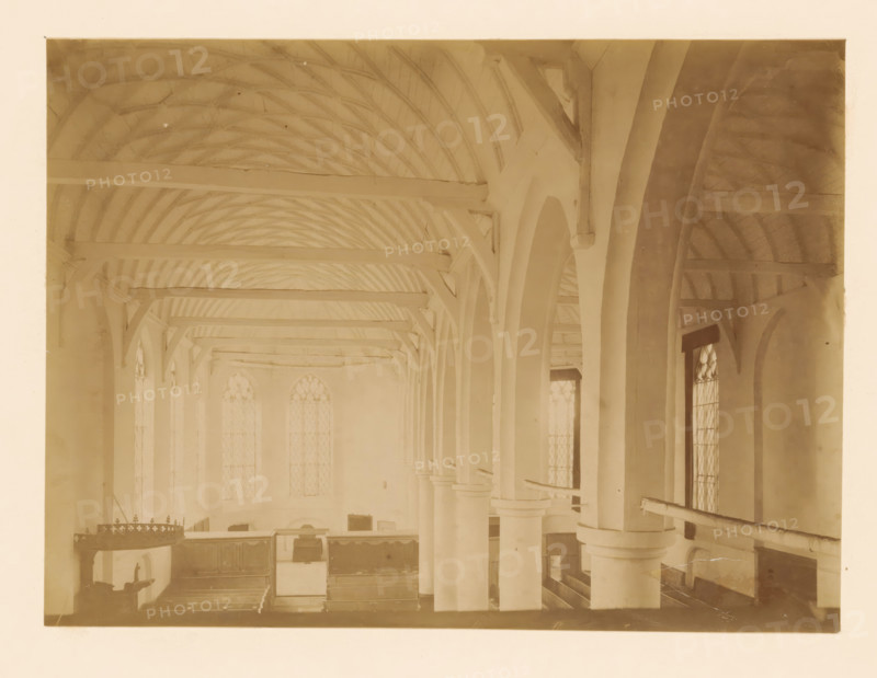 Interior of the large church in Vollenhove, photograph, annotation: 'Interior of the large church in Vollenhove (O.IJ.) Aug 1898', annotation: 'Vollenhove', Vollenhove, 1898, photographer, Attributed to, paper, pasteboard, albumen print, height 167 mm x width 230 mm, interior of church, A sepia-toned interior view showing a vaulted wooden ceiling with exposed curved beams and horizontal rafters, tall arched openings supported by round columns with capitals, narrow tall windows with patterned panes set between the arches, wooden gallery rails and pews visible below, a hanging ornate circular chandelier on one side, and various wooden panels and furnishings along the back wall.